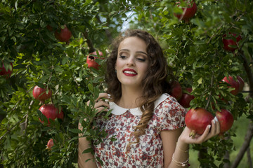 Young woman wearing floral long dress standing against pomegranate trees