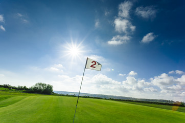 View of a green golf course, hole and flag on a bright sunny day. Sport, relax, recreation and leisure concept. Summer landscape with sunbeams