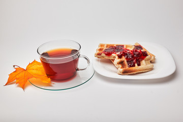 A cup of tea and crispy wafers./A cup of tea and crispy wafers poured with raspberry jam. White dishes. White background.