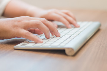 Close-up hand typing  white keyboard on wooden table