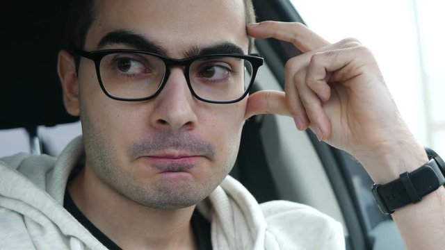 Closeup short of a young man inside a car showing signs of frustration.
