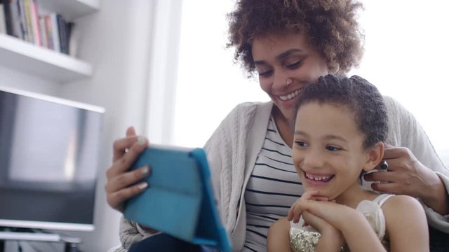Young woman with a young child laughs as they watch something together on a digital tablet, in slow motion