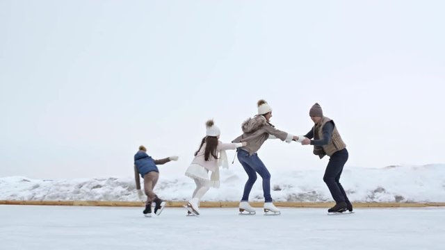 Tracking of cheerful man pulling happy woman and children skating in train formation on outdoor ice rink