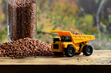 A small yellow toy truck is loaded with brown grains of buckwheat around the buckwheat pile and a...