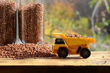 A small yellow toy truck is loaded with brown grains of buckwheat around the buckwheat pile and a...