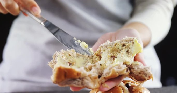 Woman applying butter over multigrain bun 