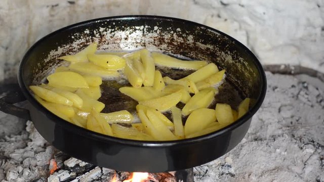 Woman fries a potato on the campfire.