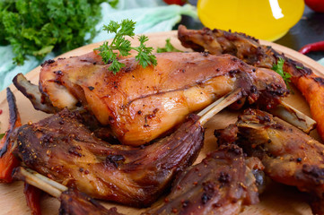 Fried pieces of rabbit with vegetables on a wooden tray on a dark background.