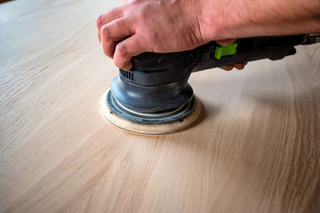 Man sanding wood with orbital sander in a workshop