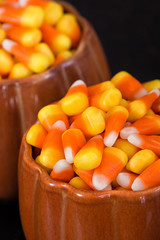 Pumpkin cups filled with Halloween candy corn. Closeup with dark background.