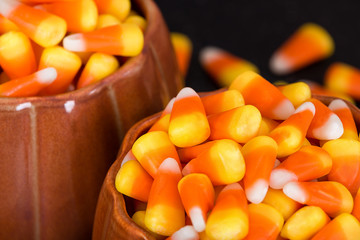 Pumpkin cups filled with Halloween candy corn. Closeup with dark background.