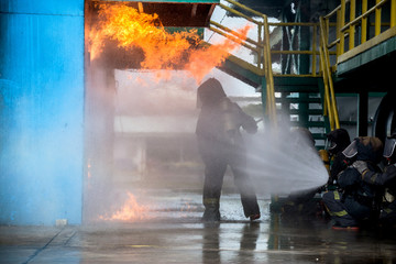 Firemen using water from hose for fire fighting at firefight training of insurance group. Firefighter wearing a fire suit for safety under the danger case.