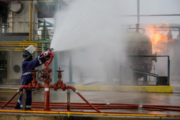 Firemen using water from hose for fire fighting at firefight training of insurance group. Firefighter wearing a fire suit for safety under the danger case.