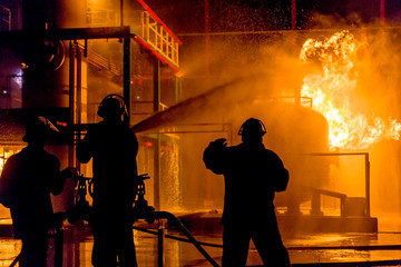 Obraz premium Firemen using water from hose for fire fighting at firefight training of insurance group. Firefighter wearing a fire suit for safety under the danger case.