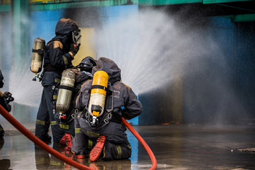 Firemen using water from hose for fire fighting at firefight training of insurance group. Firefighter wearing a fire suit for safety under the danger case.
