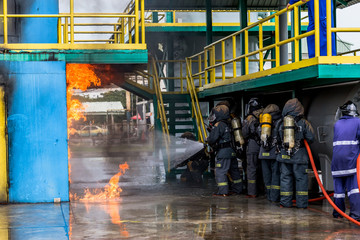 Firemen using water from hose for fire fighting at firefight training of insurance group. Firefighter wearing a fire suit for safety under the danger case.