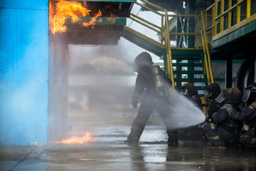 Firemen using water from hose for fire fighting at firefight training of insurance group. Firefighter wearing a fire suit for safety under the danger case.