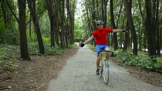 Cyclist in red blue uniform on yellow bike flies on camera revealing hands. In background passers-by.