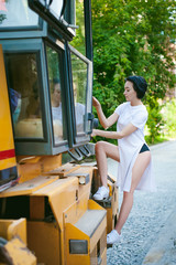 young woman with bare feet dressed in white sneakers and a long jersey, against a backdrop of urban landscapes and road machinery, asphalt paver. Street fashion.