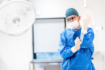 Fototapeta na wymiar Portrait of plastic surgeon wearing scrubs and protective rubber gloves in operating room
