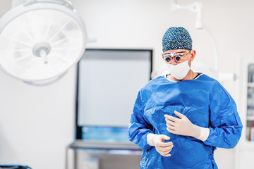 Fototapeta na wymiar Portrait of surgeon in operating theatre. Cosmetic plastic surgeon wearing scrubs, goggles and gloves getting ready for surgery