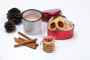 Cup of hot chocolate with cinnamon sticks, christmas cookies with jam in heart shaped red box on white background. Christmas decoration.
