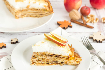 Stack of pancakes filled with apple, walnut, jam. Meringue on top. One slice served on white plate.