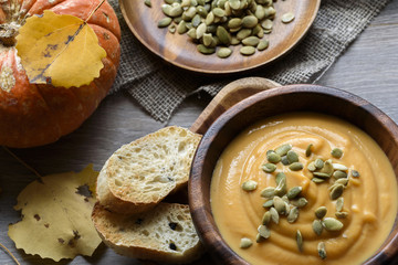 Pumpkin soup in a wooden bowl, with autumn leaves and pumpkin
