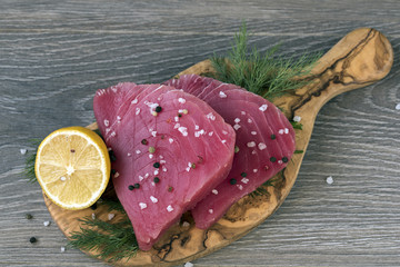Raw tuna fillet with dill, lemon and peppers in olive cutting board