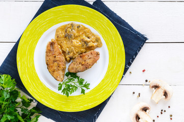 Roasted carp steaks with mushroom sauce on a plate on a white wooden background. Top view. Dish from the river fish.