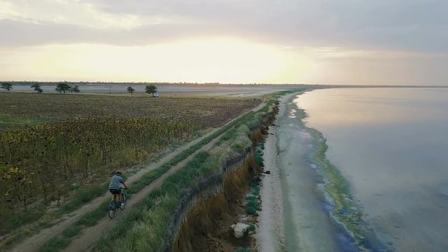 aerial footage of man riding a bicycle near the beautiful lake during sunset