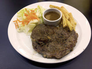 Black pepper meat steak with gravy sauce, french fries and salad in the white plate.