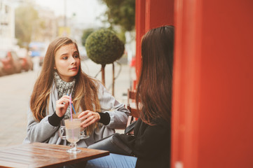 two happy girl friends talking and drinking coffee in autumn city in cafe. Meeting of good friends, young fashionable students with natural make up.