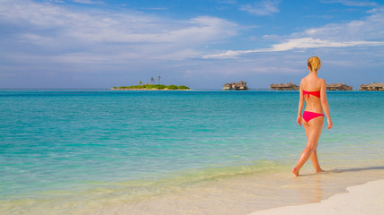 Happy beautiful carefree woman enjoying sunshine on the beach. Young woman in sexy red pink bikini in white sandy beach at Maldives. Beautiful woman's body in sexy bikini over beach background