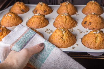 A woman pulls out Christmas cupcakes from a hot oven