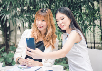 Two pretty young woman taking selfie from hand with smart phone and smiling in the garden, Urban life concept.