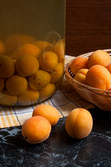Fresh organic harvested apricots in basket and big glass jar with canned apricot compote on dark marble..