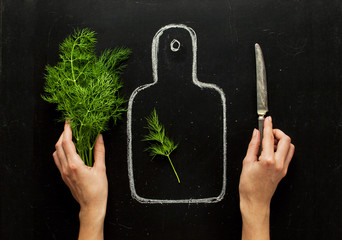 Concept of healthy eating, process of cooking, a healthy lifestyle. Hands of a woman, fresh dill on a hand-drawn cutting board, knife on a black background top view.