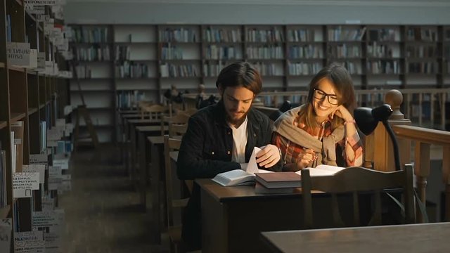 Students couple, man and girl, have study friendly discussion in the libraryhall with bookshelves, indoor dusk slowmotion