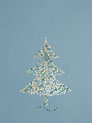 Sparkling Christmas tree made of gold stars sequins and green shiny pebbles on blue. Holiday background. New Year greeting card. Minimal