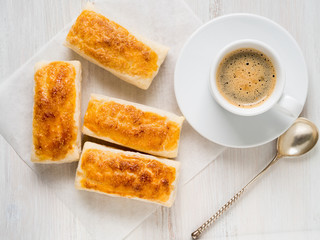 morning Breakfast with fresh rolls of puff pastry and Cup of coffee on white wooden table. Top view, the light of day.