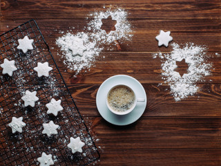 A cup of coffee and star shaped cookies on rustic background