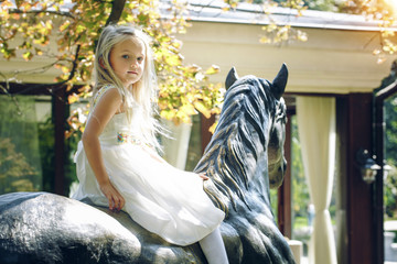 Fototapeta na wymiar Portrait of cute little blond girl on an iron horse, summertime