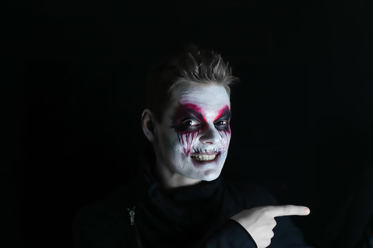 male makeup halloween on a dark background shows a finger to the side