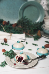 Obraz na płótnie Canvas Mini french mousse cake with berry filling and blue chocolate on white wooden table decorated plate set fir tree pine cones cups and spoon. Holiday traditional sweet dessert. Winter atmosphere food