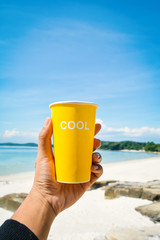 Female hand holding yellow cup with cool word  sea and blue sky background ,concept time to vacation