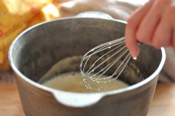 Female hand is whisking batter in cast-iron bowl, close-up, selective focus. Process of cooking