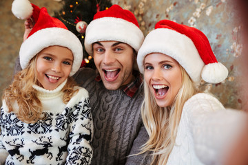 Close-up of young family in Santa's hat having fun while taking selfie