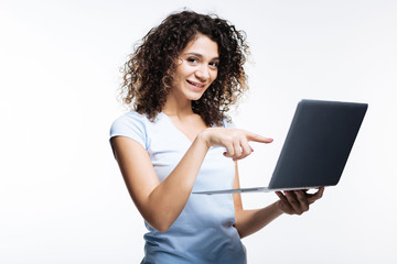 Pleasant curly-haired woman pointing at laptop