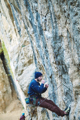 male rock climber climbs on a rocky wall at winter sunny day. Man climber in warm clothes on yellow cliff.